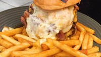 Tampilannya seperti sajian burger, tetapi ini adalah sandwich raclette yang dilumuri dengan lelehan keju. Biasanya diisi dengan berbagai isian seperti daging prosciutto dan diberi mustard. Sandwich ini mirip burger karena disajikan dengan kentang goreng. Foto: Istimewa
