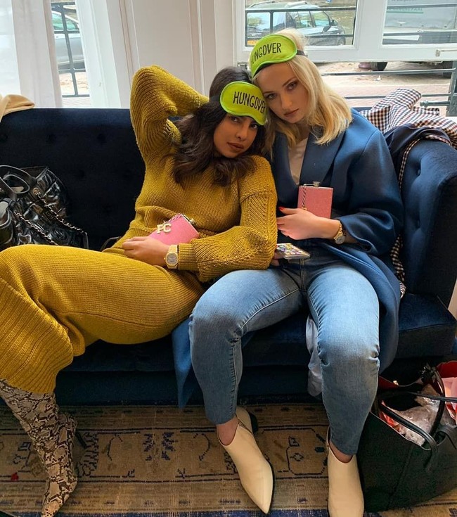 Gaya santai Priyanka Chopra memakai sweater dress warna kuning mustard usai menggelar pesta lajang. Ia tampak berpose dengan Sophie Turner yang tampil monokrom memakai jeans dan mantel biru. Foto: Instagram/@priyankachopra