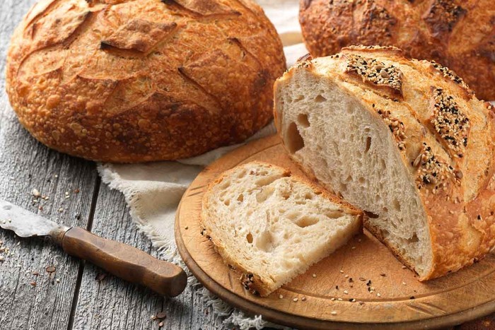 Freshly baked sourdough spelt bread and traditional italian bread on olive wood board