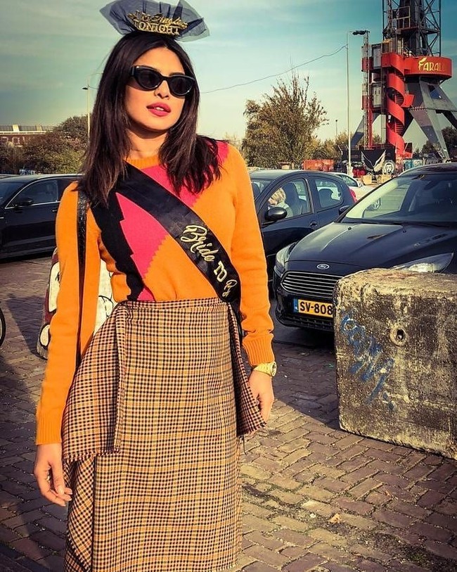 Masih menikmati liburan dan pesta lajang di Amsterdam, Belanda, Priyanka Chopra memilih busana yang lebih berwarna dengan sweater oranye-pink dipadu rok motif kotak-kotak. Terlihat ornamen pesta lajang seperti selempang hitam bertulisan Bride To Be dan headpiece warna senada. Foto: Instagram/@priyankachopra