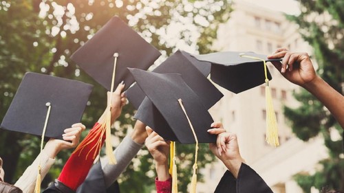 A group of multietnic students celebrating their graduation by throwing caps in the air closeup. Education, qualification and gown concept.