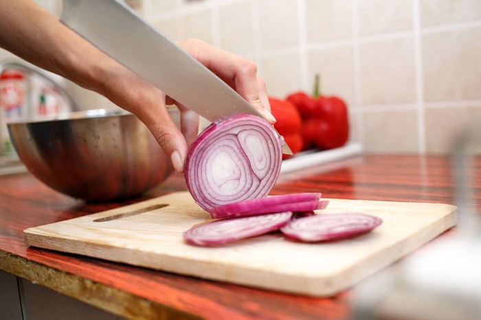 Womans hand cut red onions on cutting board in home kitchen