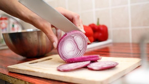 Womans hand cut red onions on cutting board in home kitchen