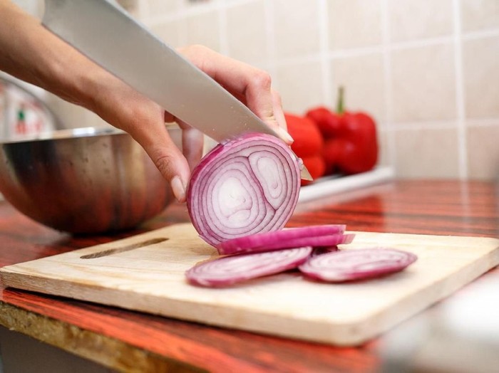 Womans hand cut red onions on cutting board in home kitchen