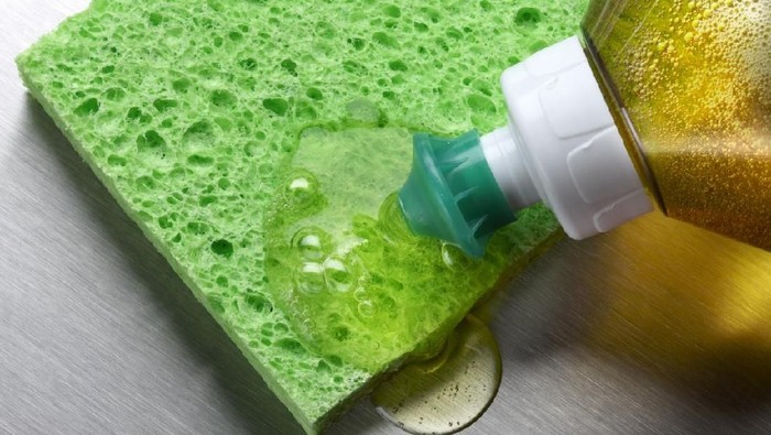 macro shot of dish soap being squeezed onto green sponge in aluminum sink