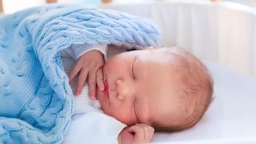Newborn baby in hospital room. New born child in wooden co-sleeper crib. Infant sleeping in bedside bassinet. Safe co-sleeping in a bed side cot. Little boy taking a nap under knitted blanket.