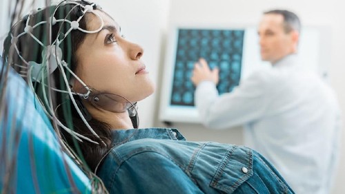 Vital procedure. Beautiful dark-haired woman lying on an examination table and undergoing electroencephalography while her doctor examining CT results