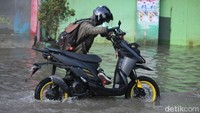 Salah seorang warga mendorong motornya di jalan yang terendam banjir.