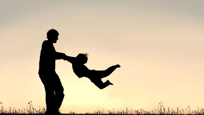 Silhouette of a happy father holding his little childs arms and spinning him in circles on a summer day.