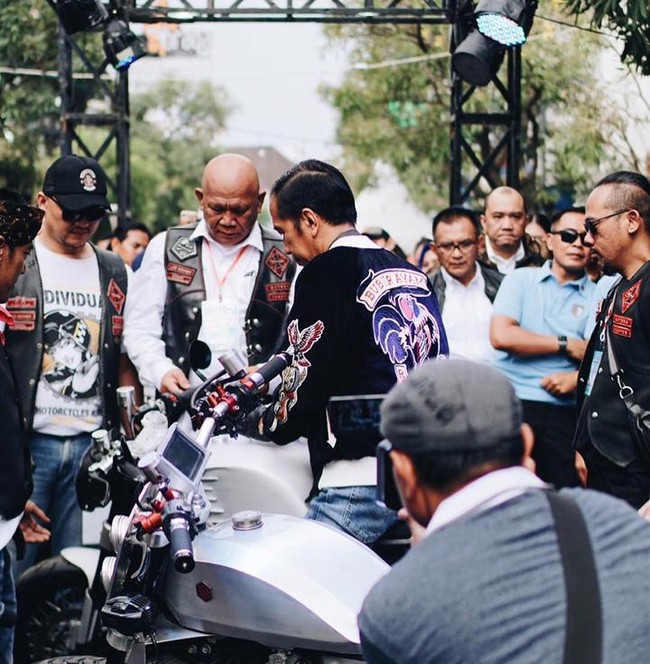 Ditengok di Instagram label tersebut, @rawtyperiot_co., jaket hitam keemasan model bomber ini terbuat dari bahan sutra silk dan velvet, dengan detail bordiran di bagian depan, lengan, dan belakang. Di bagian dada sebelah kiri terdapat tulisan Bur-Yam-Cer RTR. Sementara di bagian kirinya terdapat gambar roda dengan bendera racing (kotak-kotak hitam-putih). Di bagian belakangnya bertuliskan Bubur Ayam Racer, berikut gambar ayam. Sementara kedua lengan masing-masing dihiasi gambar ayam beserta roda yang berapi. (Foto: Instagram/@rawtype_riot)