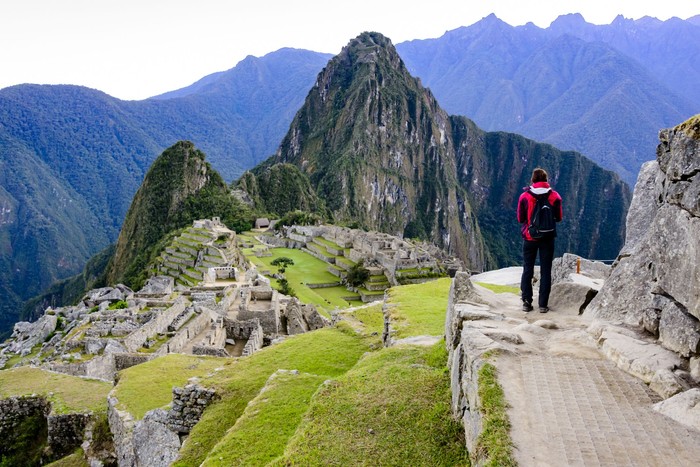 Woman standing on a ledge and overlooking the Inca ruins of the city of Machu Picchu seen in the background.