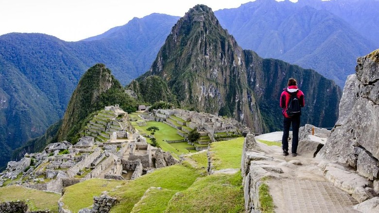 machu picchu Woman standing on a ledge and overlooking the Inca ruins of the city of Machu Picchu seen in the background.
