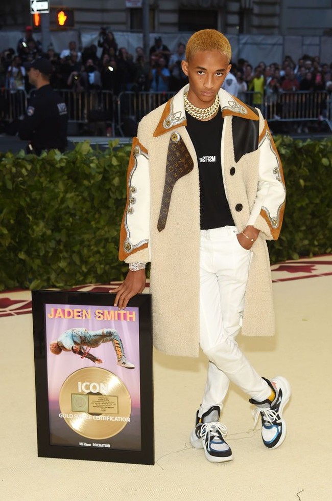 Menghadiri Met Gala 2018, Jaden Smith juga tetap dengan merek busana favoritnya, Louis Vuitton. Kali ini dia memadukan trench coat Louis Vuitton dengan kaus dari label busananya sendiri MSFTS. Dan salah satu penampilannya yang menarik atensi hari itu adalah, Jaden membawa plakat penghargaan untuk singlenya Icon. Aksesori yang unik untuk dibawa kemanapun di Met Gala. Foto: Getty Images