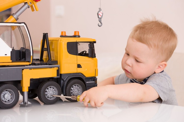 Portrait of adorable smiling toddler boy sitting at the table playing with a big construction car at home. Little child with toy car. Educative toys for children. Early learning and developing concept