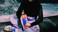 Stylish dan keren, Cella tetap tidak bisa melepaskan gurihnya keripik kentang dengan pemandangan akuarium besar di belakangnya. Foto: Instagram @cindercella