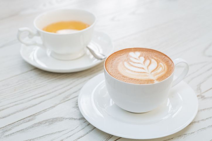 a cup of hot latte art coffee on wooden table with tea