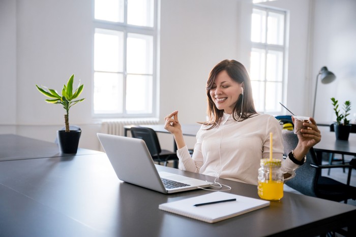 Young cheerful businesswoman listening music in headphones at office.