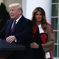 Melania Trump memakai coat panjang warna khaki dengan motif geometris berwarna merah, putih dan hitam yang bergaya retro. Coat ini tampil standout sebagai paduan serba hitam untuk gaun dan boots dari Christian Louboutin. Foto: Dok. Getty Images