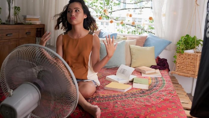 kipas angin Sweating Asian girl cooling herself with big fan