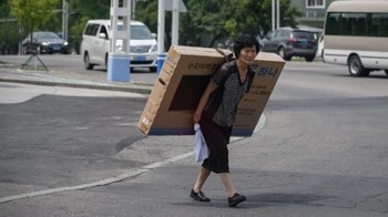 Tengok aksi perempuan paruh baya ini memanggul boks televisi layar datar, bukan lagi televisi layar cembung alias CRT. Oke, memang belum tentu ada televisi di dalam boks tersebut. (Foto: Ed JONES/AFP)