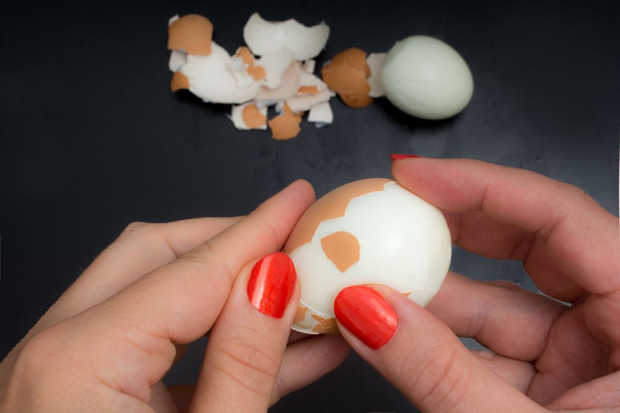 pov woman peeling a boiled chicken egg with her hands on dark kitchen dresser