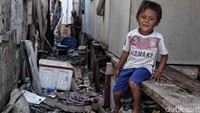 Seorang anak duduk di rumah panggung yang di bawahnya banyak sampah yang berserakan.