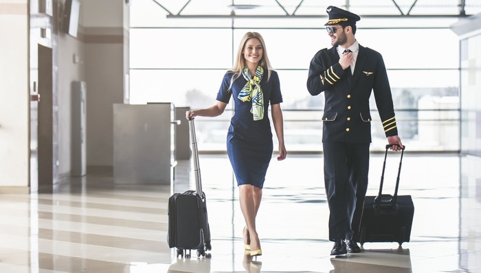 Handsome male pilot and attractive female flight attendant are walking in airport terminal together.