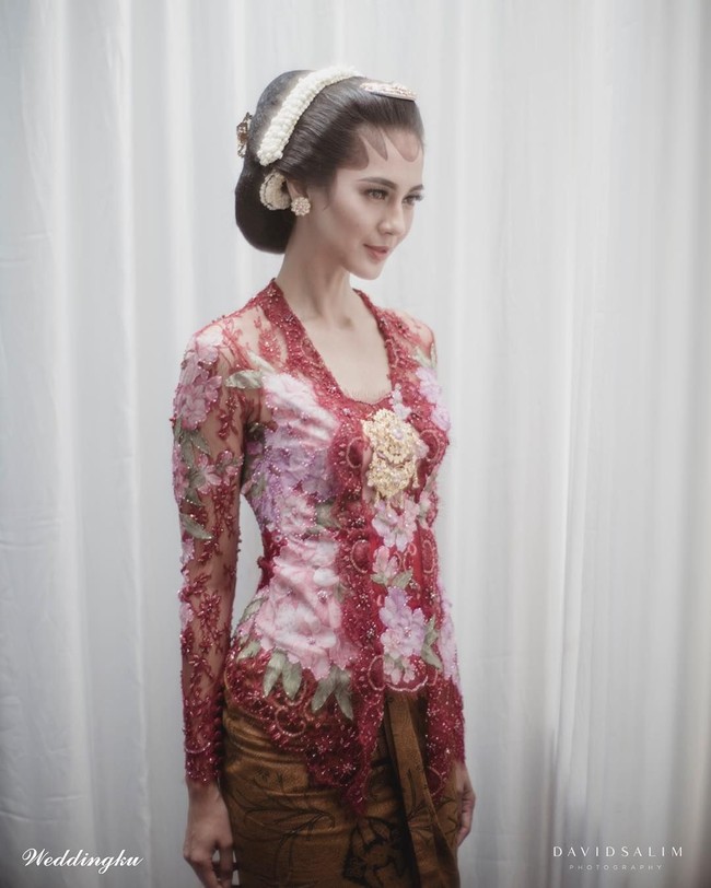 Ketika melakukan ritual adat siraman, pilihan kebaya tampak lebih berani dengan nuansa merah rancangan Poppy Karim. Kebaya model kutubaru tersebut tampil mencuri atensi dengan motif bunga bernuansa pink sebagai padanannya. Foto: Dok. David Salim Photography