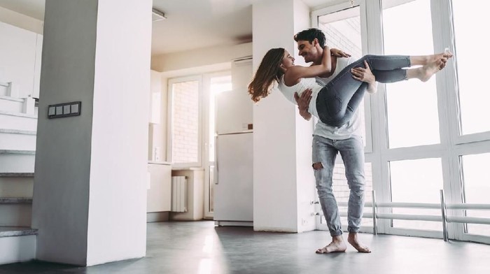 Romantic couple at home. Attractive young woman and handsome man are enjoying spending time together. Sitting on the floor in light modern kitchen.