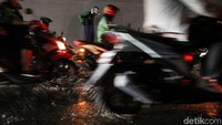 Seorang pengendara sepeda motor tampak memakai jas hujan di kolong Semanggi.