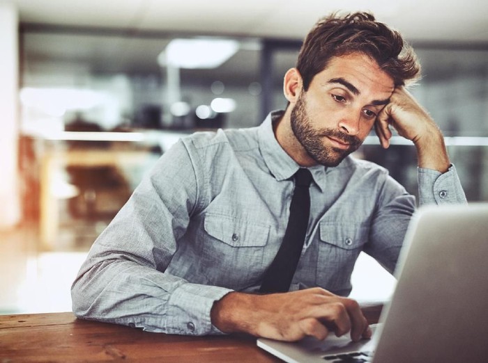 pria bekerja, Shot of a handsome young businessman looking bored while working on a laptop in an office
