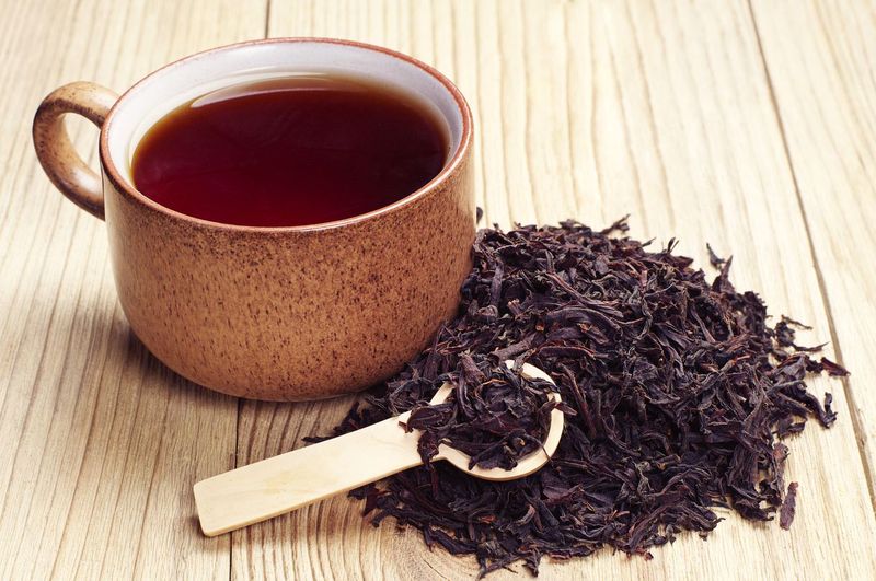 475614605 Black tea in a cup and dried leaves on wooden background