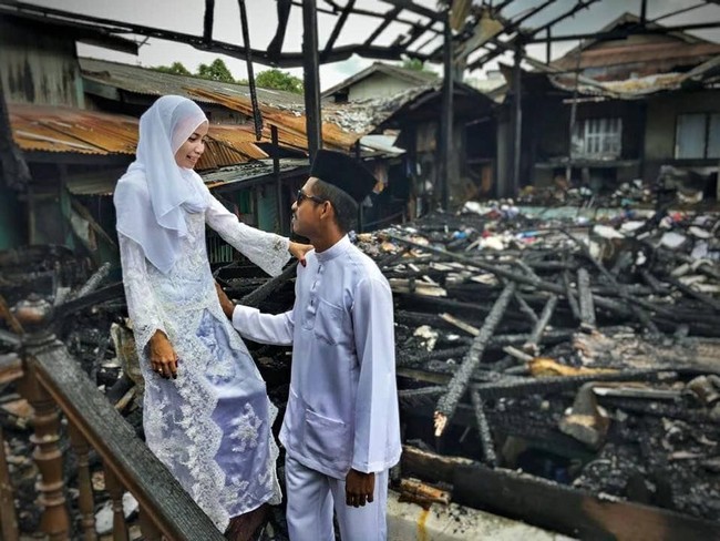 Pasangan ini kemudian memutuskan melakukan foto pernikahan di depan rumah yang hangus terbakar. Hasmi tampil anggun dalam balutan  gaun pengantin bernuansa putih dan hijab gaya simpel. Foto: Facebook Asmieyz Zahariey