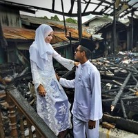 Pasangan ini kemudian memutuskan melakukan foto pernikahan di depan rumah yang hangus terbakar. Hasmi tampil anggun dalam balutan  gaun pengantin bernuansa putih dan hijab gaya simpel. Foto: Facebook Asmieyz Zahariey