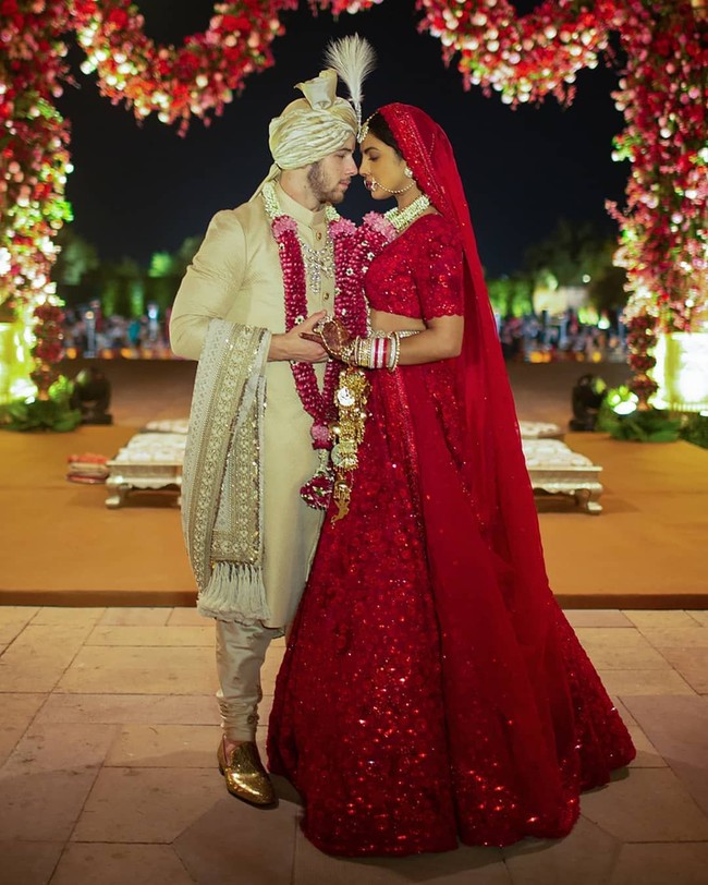 Dalam foto lain, istri Nick Jonas tersebut juga terlihat memakai busana tradisional India yakni choli dan lehenga berwarna merah yang dipadukan dengan dupatta berdetail renda sebagai penutup kepala. Baju tersebut pun terlihat glamour dengan materialnya yang gemerlapan. Sedangkan Nick memakai sherwani emas dengan turban berbulu. Foto: Instagram @priyankachopra