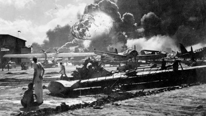 An explosion at the Naval Air Station, Ford Island, Pearl Harbour (Pearl Harbor) during the Japanese attack. Sailors stand amid wrecked watching as the USS Shaw explodes in the center background. The USS Nevada is also visible in the middle background, with her bow headed toward the left.    (Photo by Fox Photos/Getty Images)