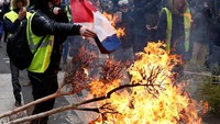 Seorang pengunjuk rasa mengenakan rompi kuning membakar bendera Prancis di barikade saat bentrokan dengan polisi (Foto: Reuters)