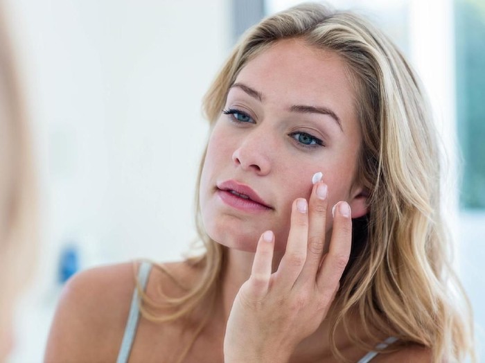 846330444 Smiling pretty woman applying cream on her face in bathroom