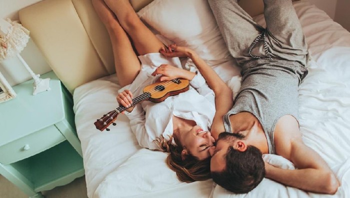 Lovely couple in pyjamas spending morning in their bed, celebrating Valentines day by playing an ukulele