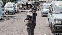Dengan memanggul batang bambu berisi air aren dia berjalan menyusuri terminal yang ramai oleh lalu lalang kendaraan.