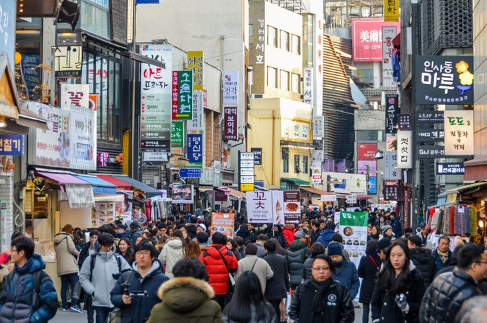 A crowded street in the Dongdaemun District of South Korea. There are many storefronts and people. Photo taken during a cold winter day.
