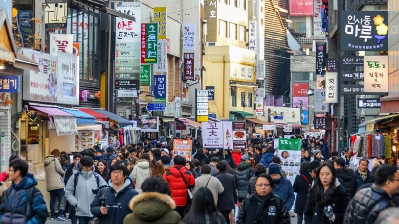 ilustrasi turis di seoul A crowded street in the Dongdaemun District of South Korea. There are many storefronts and people. Photo taken during a cold winter day.