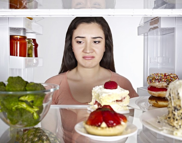 Young woman sadly looking  inside a fridge