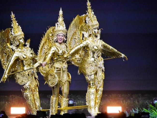 Berbeda dengan finalis lainnya, On-anong tampil tak sendirian saat memeragakan kostum nasionalnya. Dia naik ke atas panggung bersama dua boneka berwarna emas yang menyatu dengan dirinya. Miss Laos itu pun didandani sama persis berwarna emas dengan dua boneka yang bergerak seiring gerakannya tersebut. Foto: Instagram