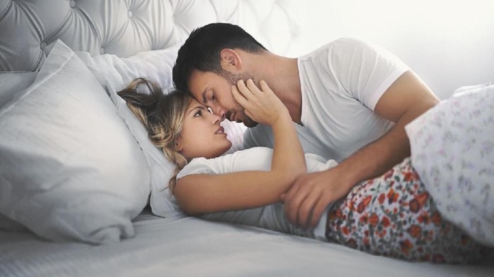 ilustrasi pasangan Closeup side view of late 20s couple kissing in bed which probably leads to some love making. They are both still wearing pajamas and everything is decent.