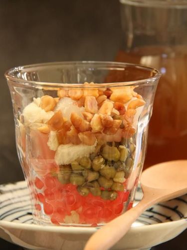 Wedang Angsle, the traditional Javanese warm dessert from Malang, East Java. Tapioca pearls, rice noodle cake, agar jelly cubes, palm fruit, mung beans, peanuts and bread cubes in warm infusion of ginger and coconut milk. The dish is plated in a ceramic deep bowl with a metal soup spoon inserted in the bowl. The dish is served with sticky rice and sesame cakes, a traditional local snack popular in the area. A batik cloth is used as a table cloth.