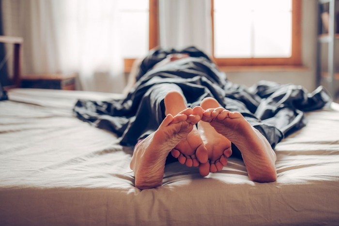 Closeup side view of late 20s couple kissing in bed which probably leads to some love making. They are both still wearing pajamas and everything is decent.
