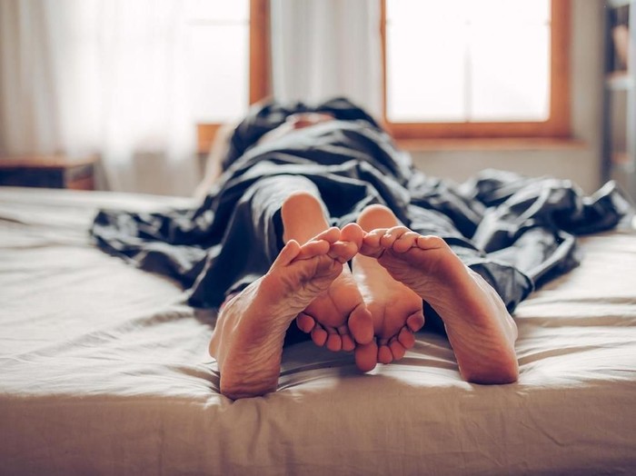 Closeup side view of late 20s couple kissing in bed which probably leads to some love making. They are both still wearing pajamas and everything is decent.