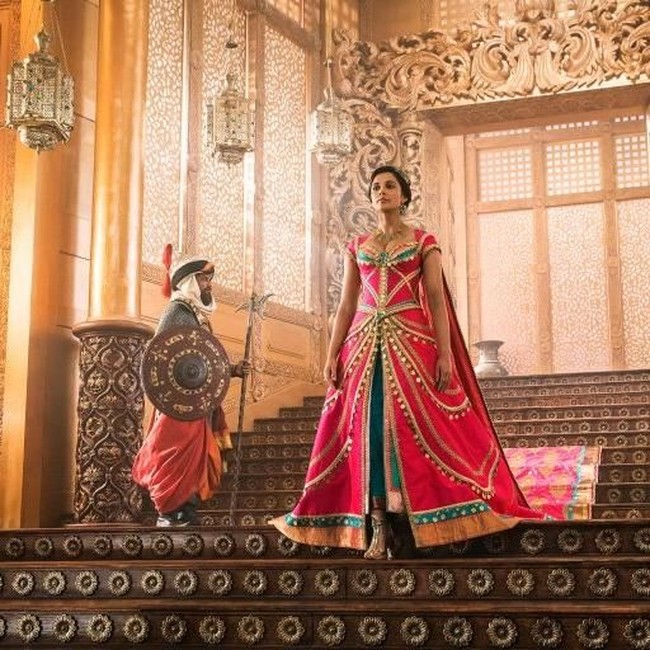 Mengenakan gaun putri kerajaan, Putri Jasmine tampak berdiri di tangga istana Sultan, ayahnya. Aura megah dan royal terpancar dari gaun berpotongan A-line warna pink-hijau. Foto: dok. Daniel Smith/Disney