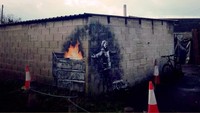 Dinding garasi mobil di pemukiman wilayah Port Talbot, Wales, juga dilukis oleh Banksy. Ia membuat gambar bocah yang sedang menikmati butiran salju tapi di sisinya ada kobaran api yang menghangatkan. Foto: Banksy/ Instagram